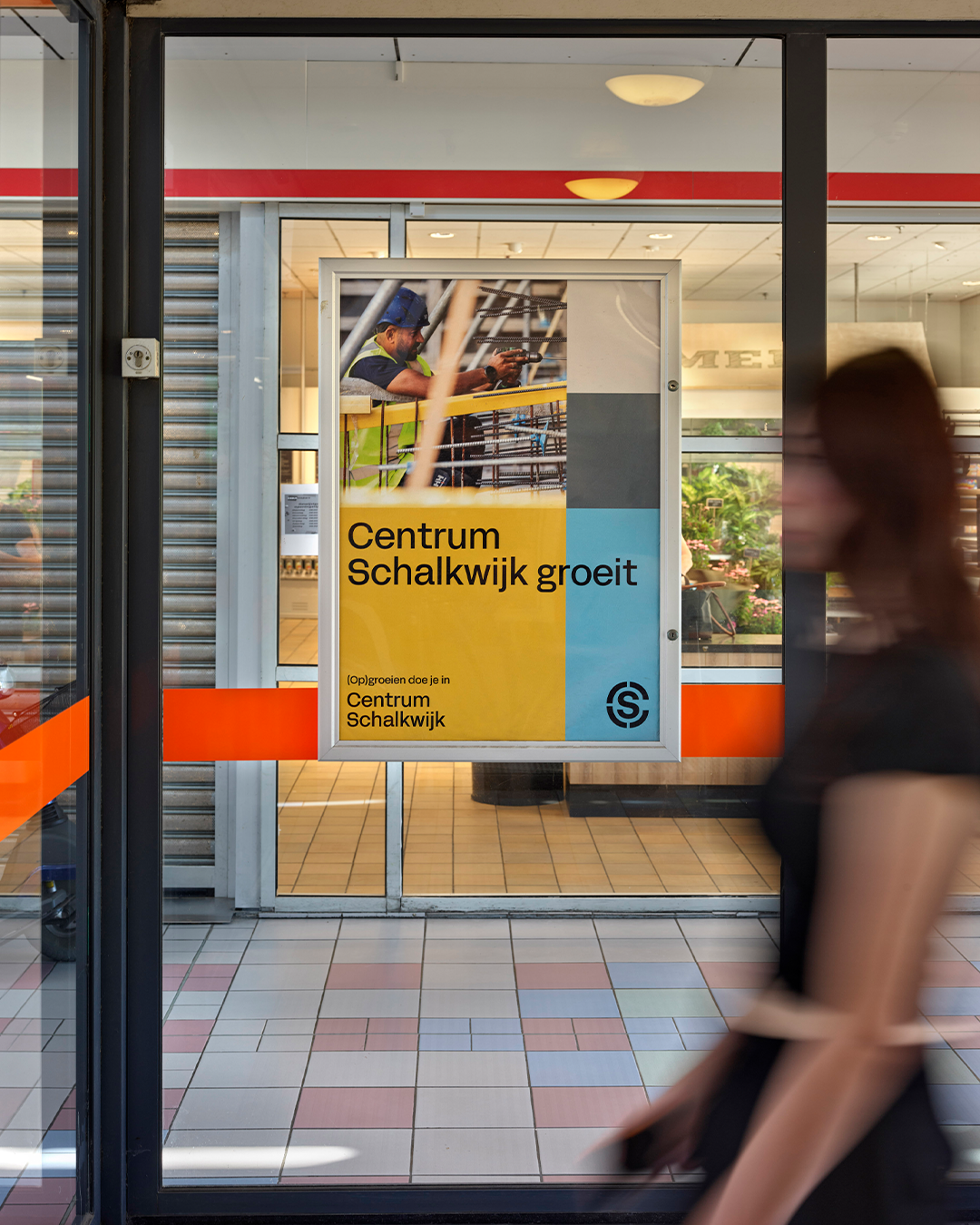 Een poster die binnen een centrumwinkel hangt waar mensen voorbij lopen